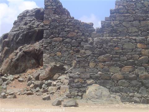 Ancient ruined lava-stone wall against volcanic rock under blue sky