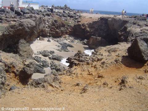 Natural pool carved in volcanic rock, tourists swimming on rocky coast