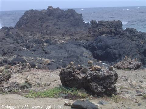 Black lava rocks on the coast, stacked pebbles in front, choppy sea behind