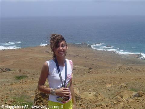 Smiling tourist standing on arid rocky coast above the ocean