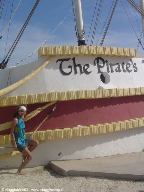 Woman posing on sand in front of the white and red ship 'The Pirate's'