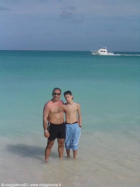 Father and son in turquoise water at Saona, a motorboat passing behind