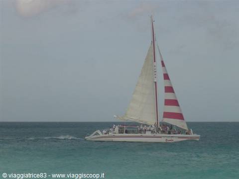 Catamaran with red striped sail carrying passengers across turquoise sea