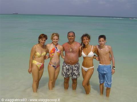 Five people in swimwear pose in the turquoise water of a tropical beach