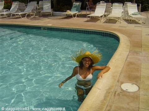 Woman in straw hat leaning on pool edge, white loungers behind