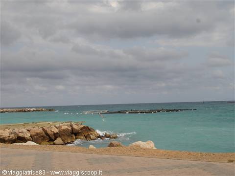 Rocky breakwater on turquoise sea, foamy waves, cloudy sky