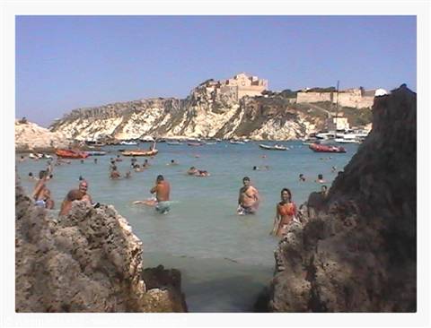 Swimmers among rocks in turquoise water, fortress perched on the cliff, Tremiti Islands