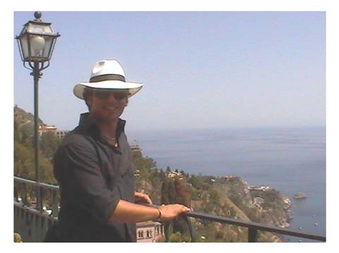 Man in white hat and sunglasses leaning on a railing above the Mediterranean coast