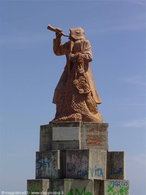 Rust-colored iron statue of fisherman blowing horn on graffiti-covered concrete pedestal