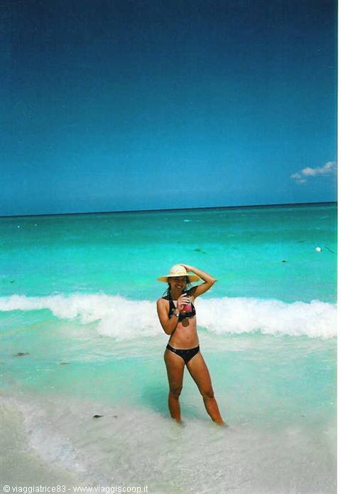 Woman in straw hat and black bikini standing in turquoise sea foam