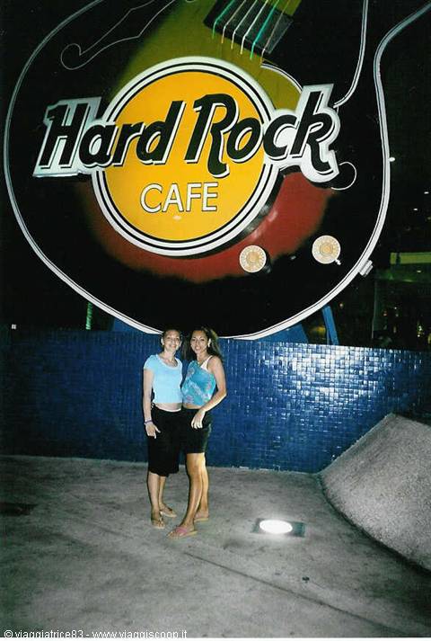 Two women posing under the guitar sign of Hard Rock Cafe at night