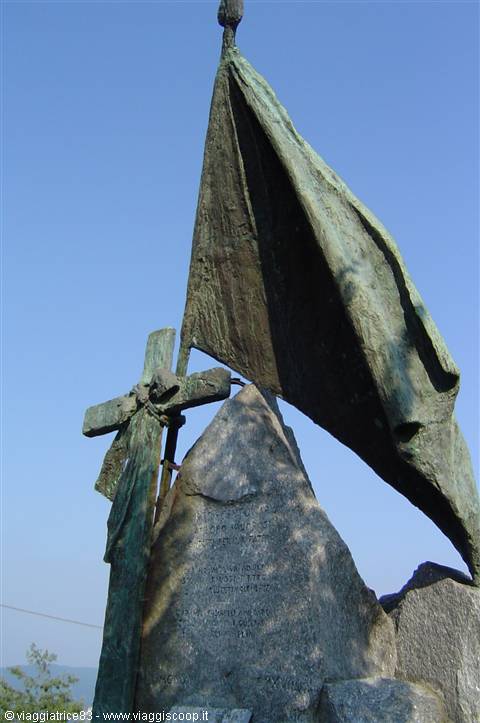 Bronze monument with flag and cross on granite boulder, blue sky
