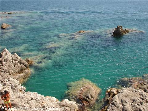 White rocks over clear turquoise sea, woman in swimsuit on rocks