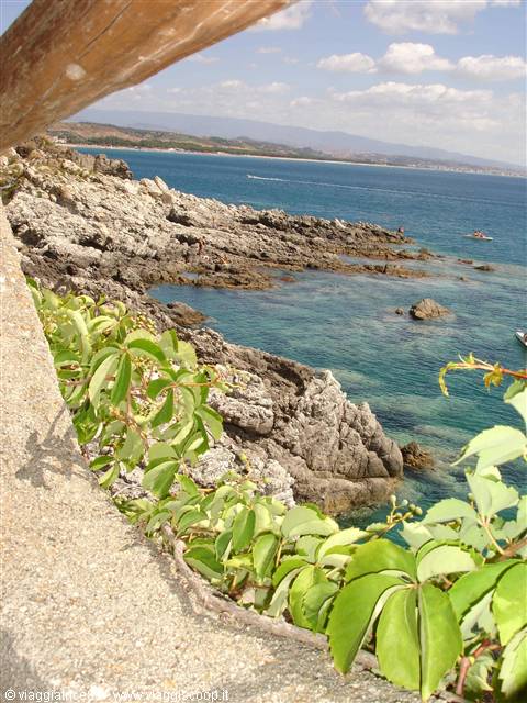 Grey rocks and turquoise water from concrete terrace, green vines in foreground
