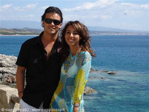 Smiling couple on rocky cliffs overlooking the blue sea