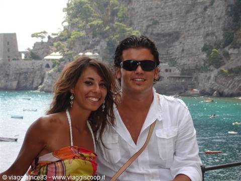 Smiling couple by turquoise sea at Praiano, cliffs and houses behind