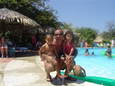 Father with two children by the pool, thatched umbrellas and swimmers around