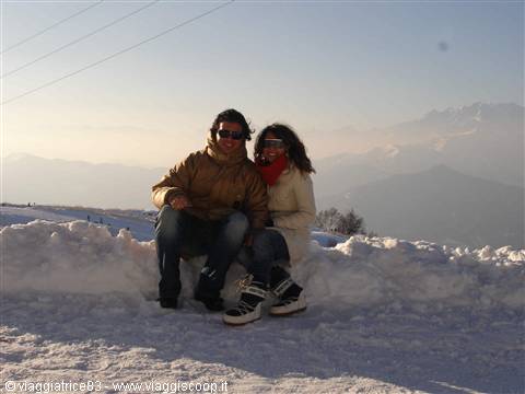 Couple sitting on snow with misty snowy mountains behind them