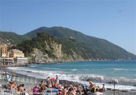 Bathers on Camogli pebble beach, colorful houses and waves under green hills