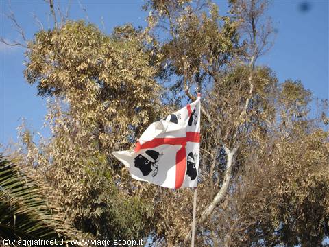 Sardinian flag with red cross and Moor heads waving against trees and blue sky