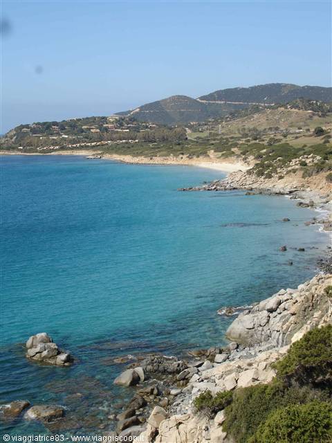 turquoise water among granite rocks and Mediterranean scrub, sandy beach in the distance
