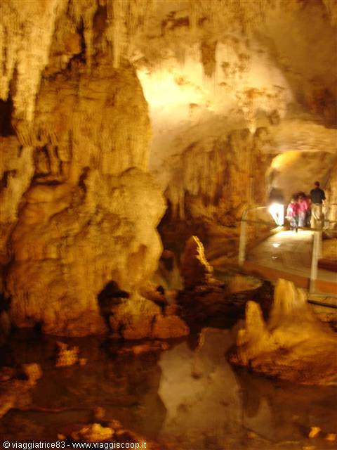Visitors on metal walkway inside cave with stalactites and lit underground lake