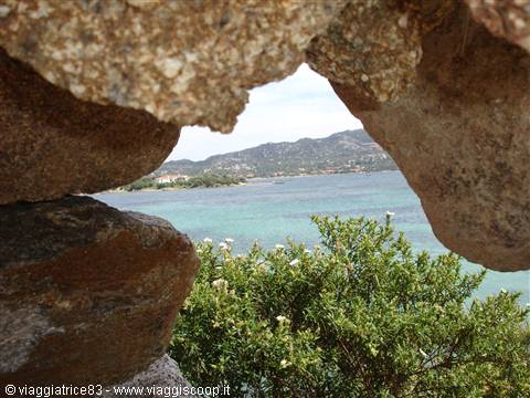 Turquoise sea and green hills framed through a hole between granite rocks