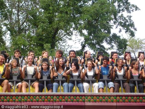 Young riders smiling on amusement park ride seats, green trees behind
