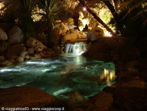 Small illuminated waterfall among rocks and palm trees at night
