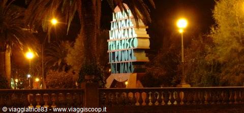 Book-shaped monument lit up at night among palm trees and street lamps