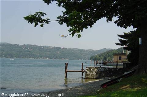 Old wooden pier on the lakeshore, boats and tree shade