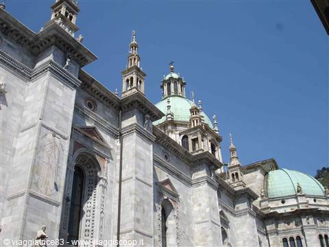 Marble facade of Como Cathedral with green domes under blue sky