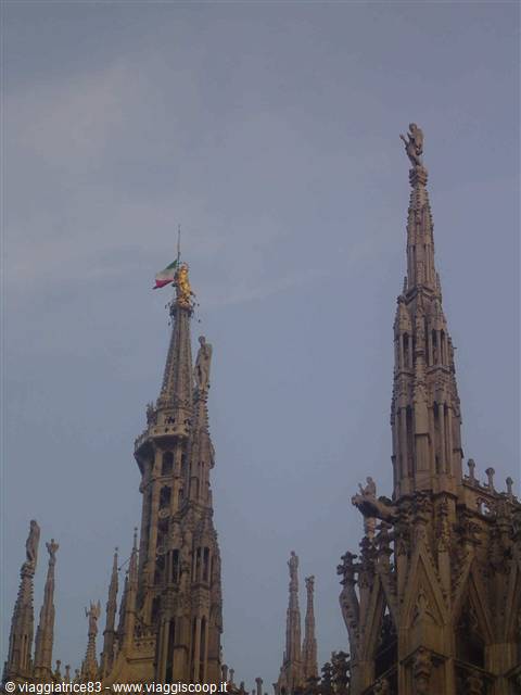 Marble spires of Milan Cathedral with golden Madonnina and Italian flag