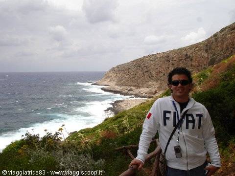 Man in white sweatshirt on a coastal trail beside rocky cliffs