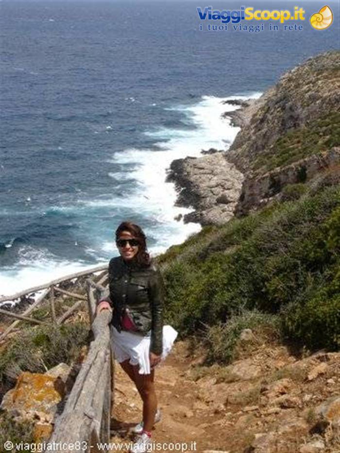 Woman in leather jacket on rocky cliff path with wooden railing above crashing waves