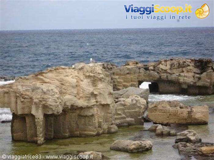 Limestone rocks on green water, a seagull resting, open sea and grey sky