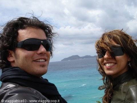 Two smiling young people in sunglasses in front of the sea and an island