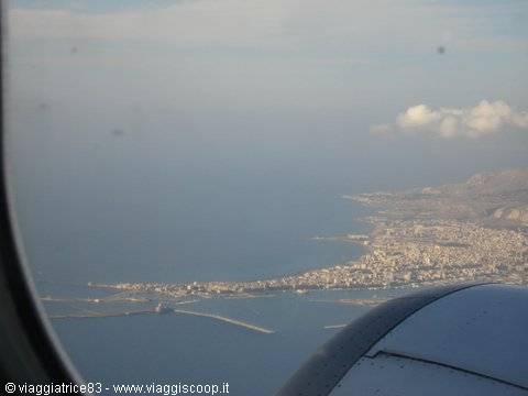 Coastal city and port seen through airplane window, engine in foreground