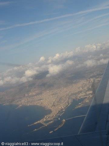 Coastal city seen from the airplane window, wing in foreground, scattered clouds
