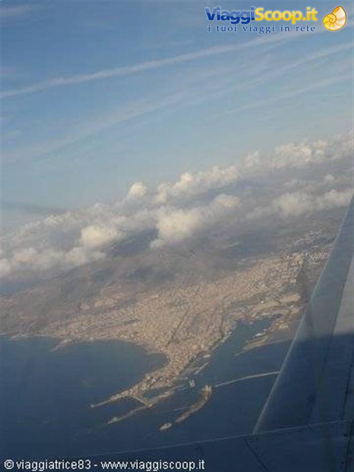Coastal city seen from the airplane window, wing in foreground, scattered clouds