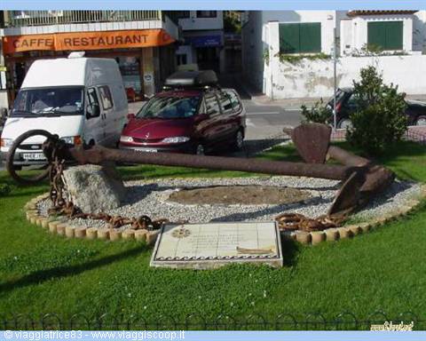 Old rusted iron anchor with chain displayed on grass with plaque