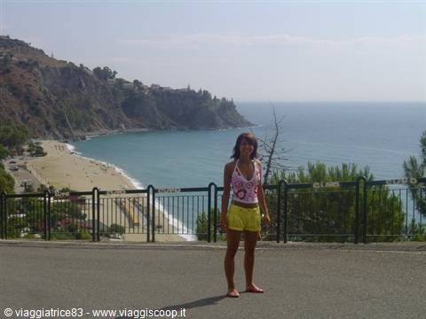 Woman in white top and yellow shorts by Taormina beach, turquoise sea