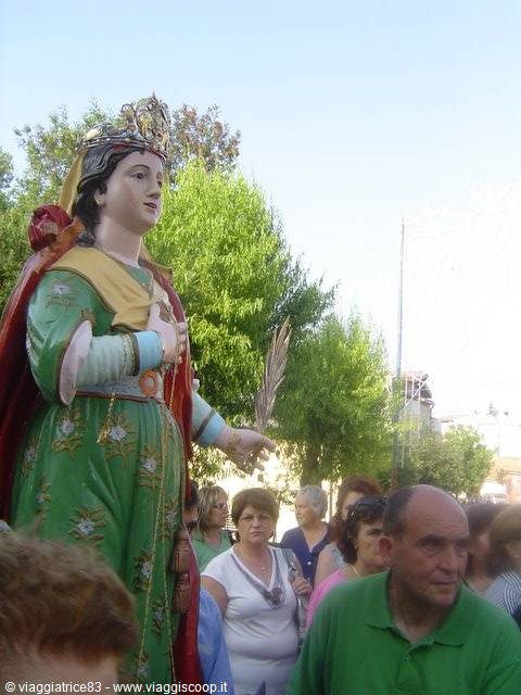 Crowned saint statue carried in procession among crowd under trees