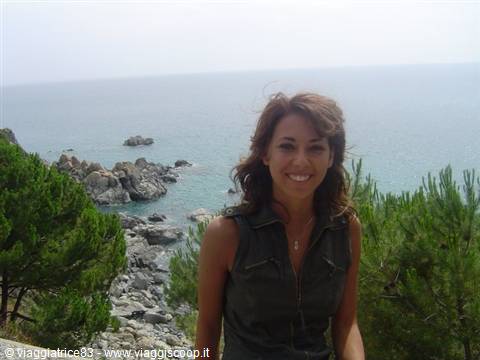 Smiling woman among pines on rocky seaside coast