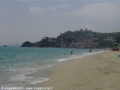Swimmers on pale sand, turquoise sea, village on green headland