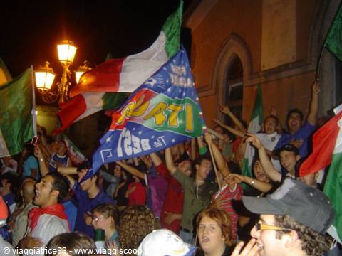 Fans cheer at night waving Italian flags and banners under streetlights