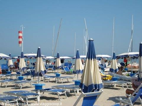 Beach with blue and white umbrellas, sun loungers and sailboat masts