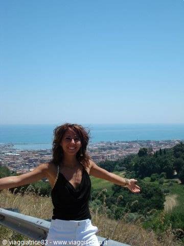 Woman with open arms in front of a city and blue sea by guardrail