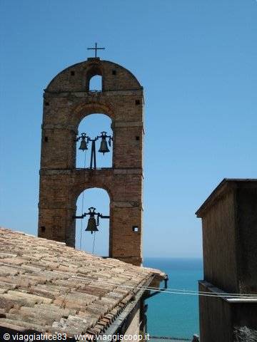 Brick bell tower with visible bells above rooftops facing the sea
