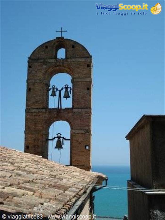 Brick bell tower with visible bells above rooftops facing the sea